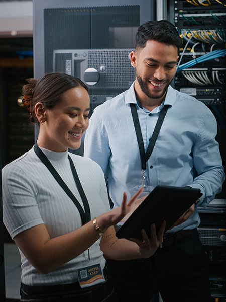 Two employees smiling while looking at the tablet inside data centre