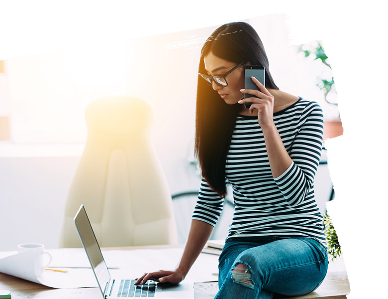 Woman talking with someone on mobile phone while working with laptop