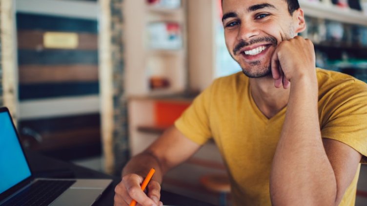 Smiling man using laptop looking back at the camera