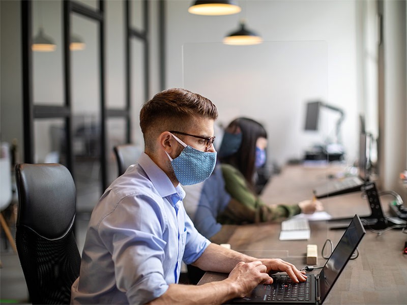 Employees working having face mask on in office workspace during COVID-19