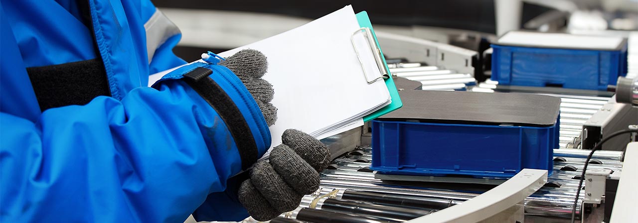 Closeup shooting hand of worker with clipboard checking plastic crate for fruits and vegetables loading on conveyor machine in cold room warehouse