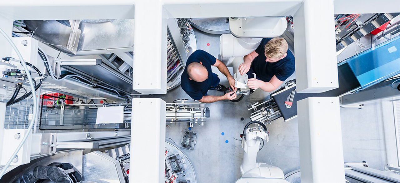 Top view of two colleagues working at industrial robot